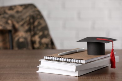 Photo of Notebooks, mortarboard and pen on wooden table, space for text. Military education