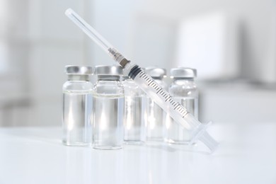 Photo of Syringe with vials of medicine on white table, closeup