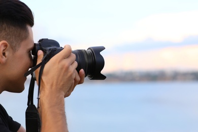 Photographer taking picture with professional camera near river, closeup