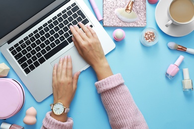 Photo of Young beauty blogger working with laptop on light blue background, top view