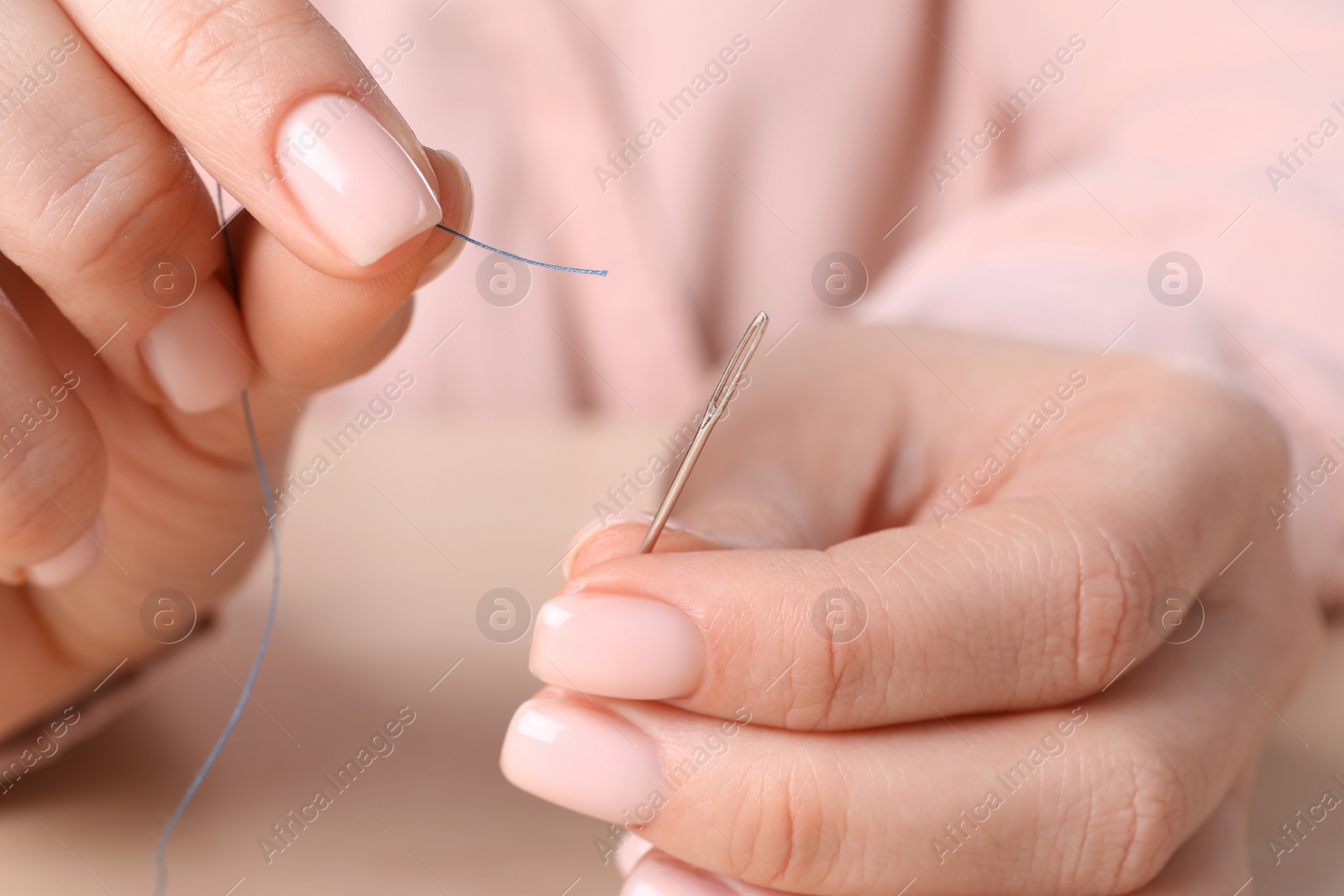 Photo of Woman threading sewing needle at table, closeup