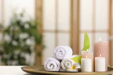 Spa composition. Burning candles, plumeria flower, green leaves and towels on white table indoors, space for text