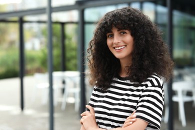 Portrait of beautiful woman with crossed arms outdoors. Attractive lady smiling and looking into camera. Space for text