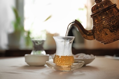 Pouring hot tea into glass cup on table