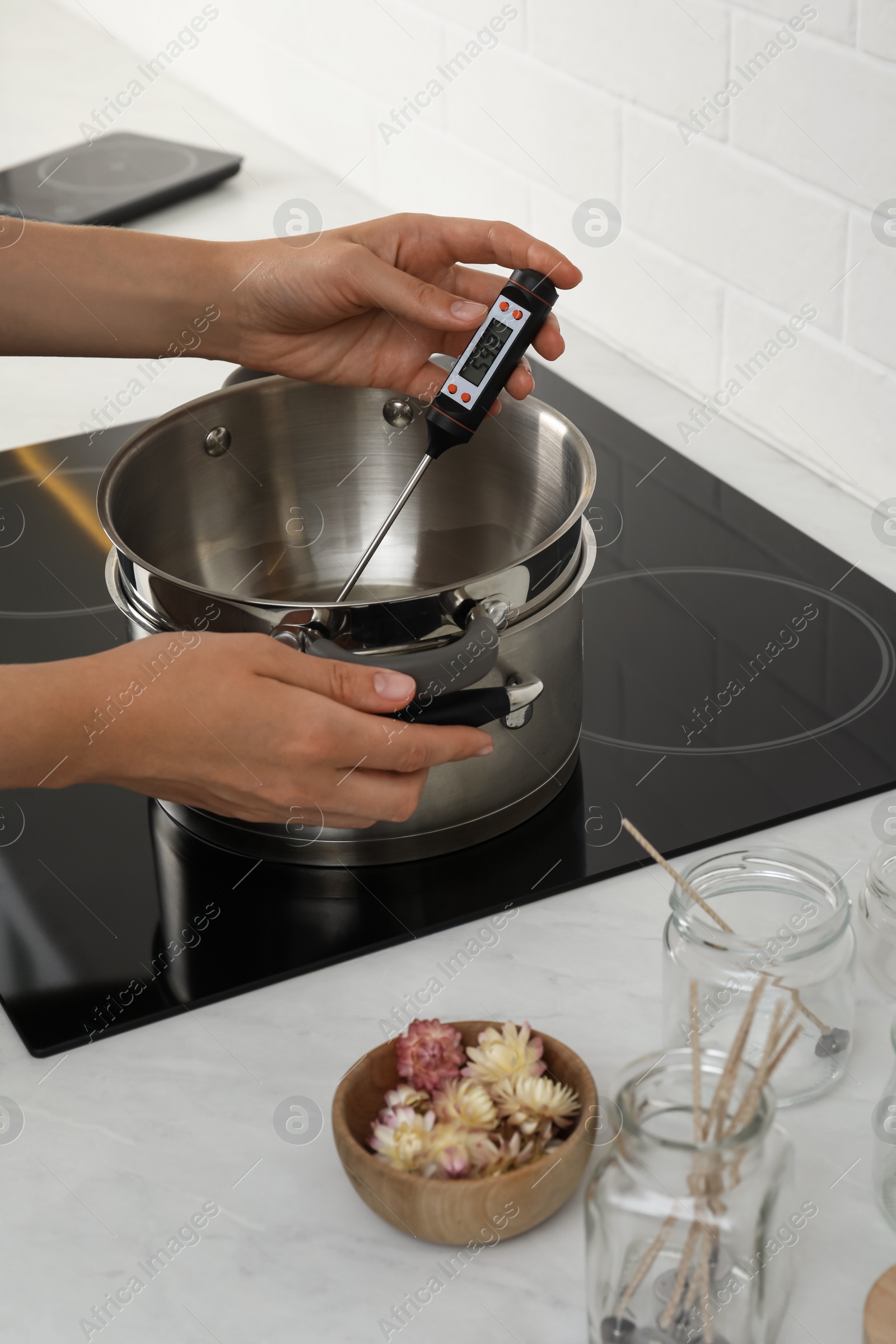 Photo of Woman measuring temperature of melted wax in kitchen, closeup. Making homemade candles