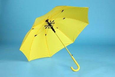 Stylish open yellow umbrella on light blue background