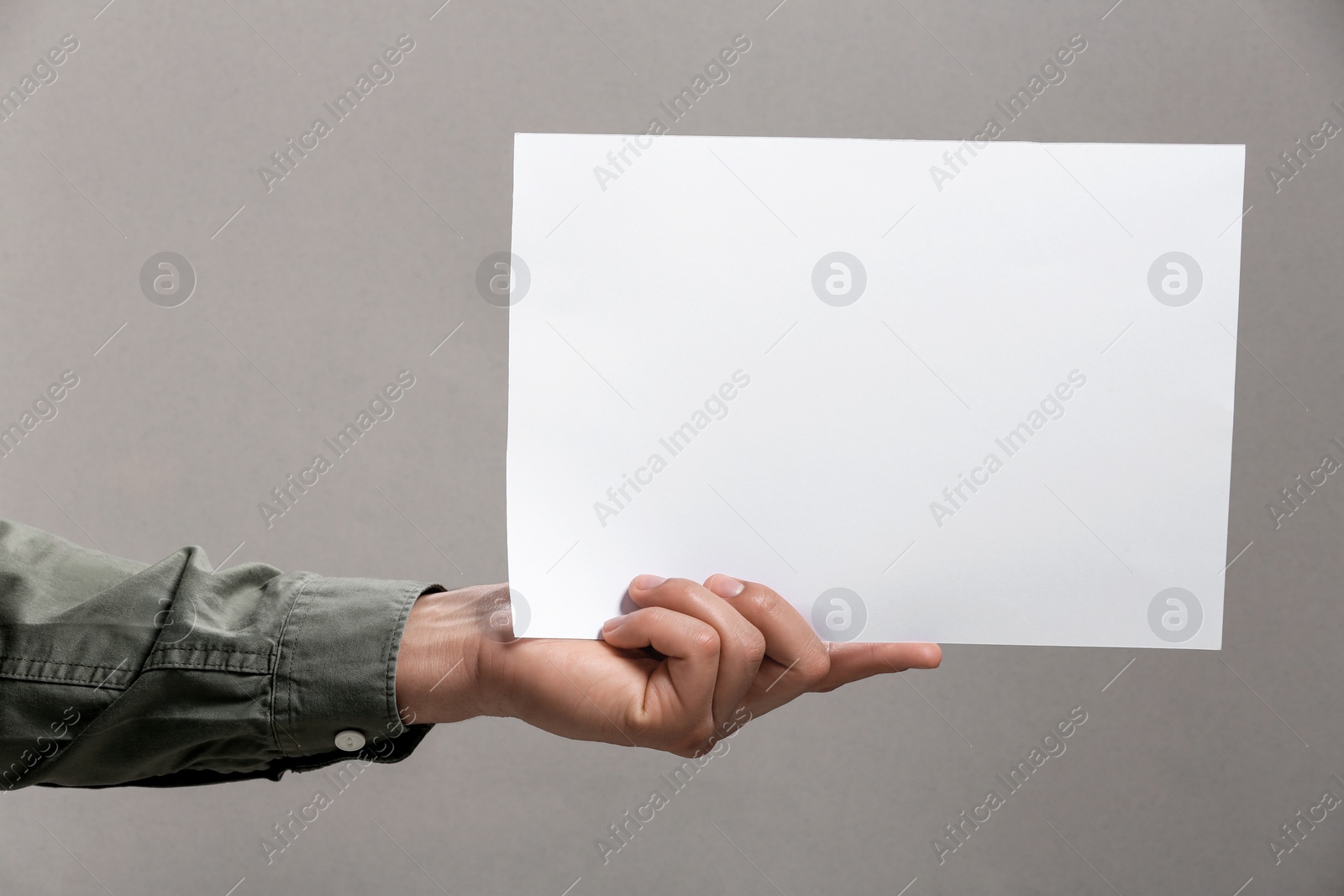 Photo of Man holding sheet of paper on grey background, closeup. Mockup for design