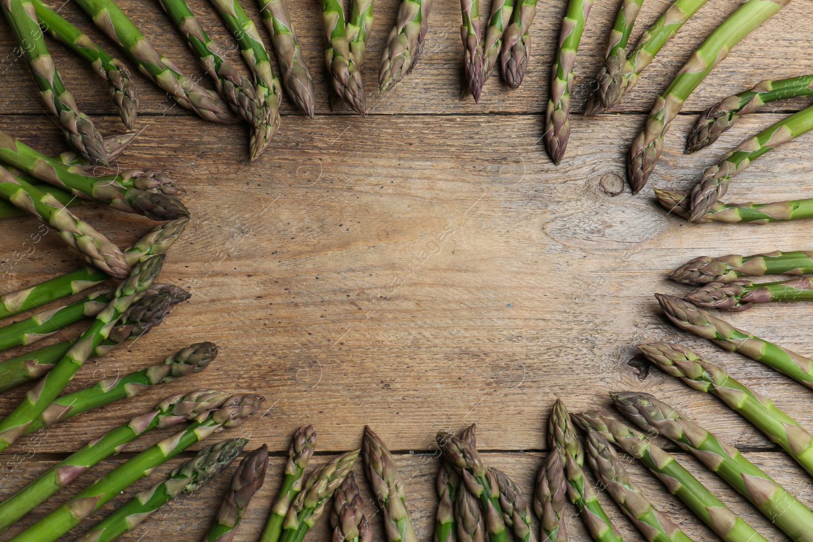 Photo of Frame made with fresh raw asparagus on wooden table, flat lay. Space for text