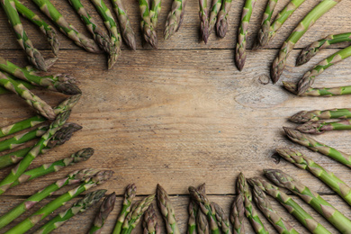 Frame made with fresh raw asparagus on wooden table, flat lay. Space for text