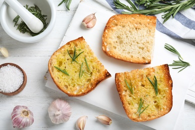 Slices of toasted bread with garlic and herb on white wooden table, flat lay