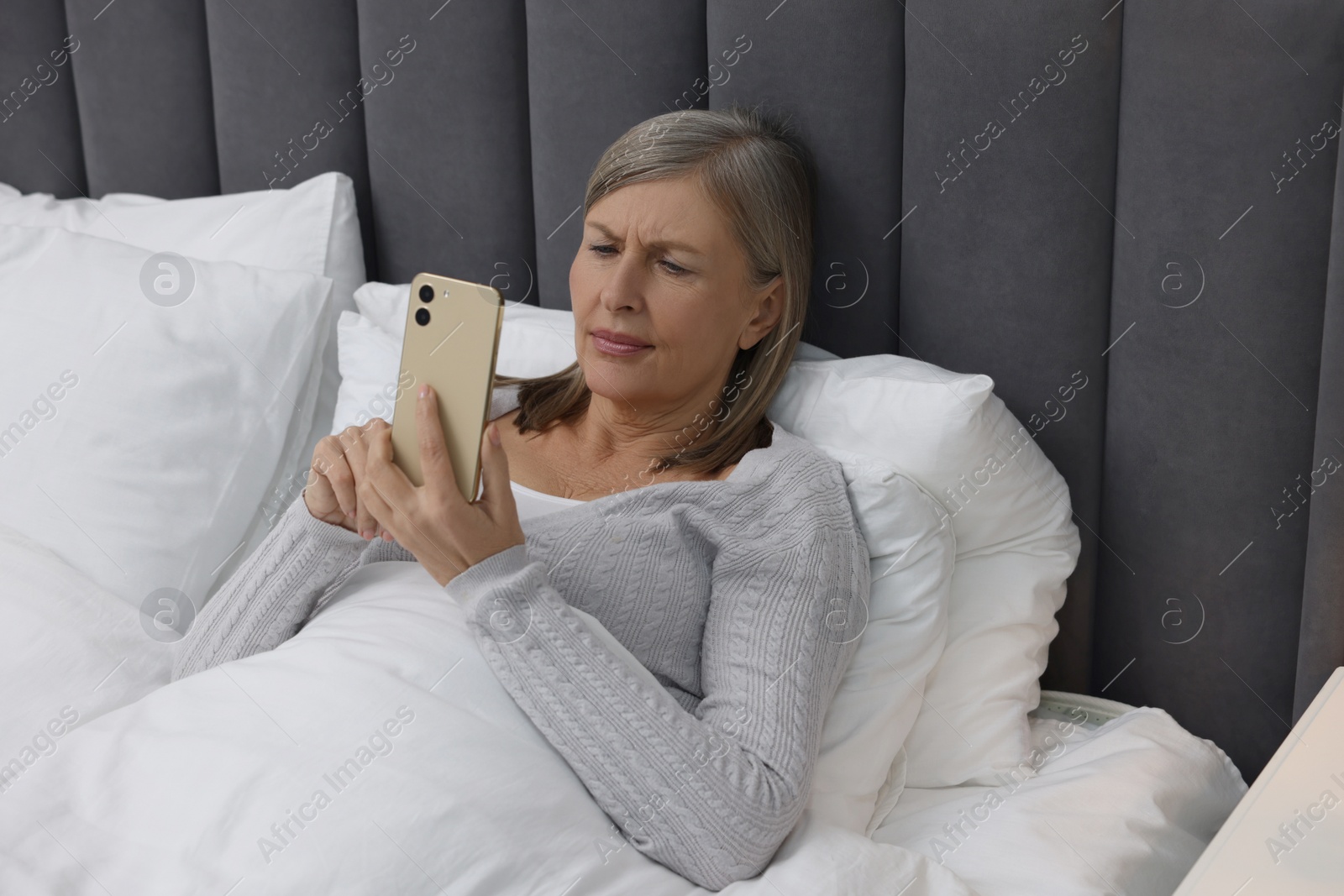 Photo of Menopause. Sleepless woman using smartphone in bed indoors