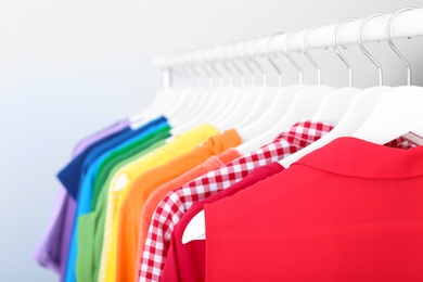 Photo of Rack with rainbow clothes on light background