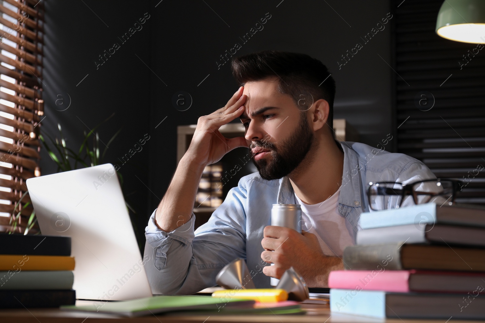 Photo of Tired young man with energy drink studying at home