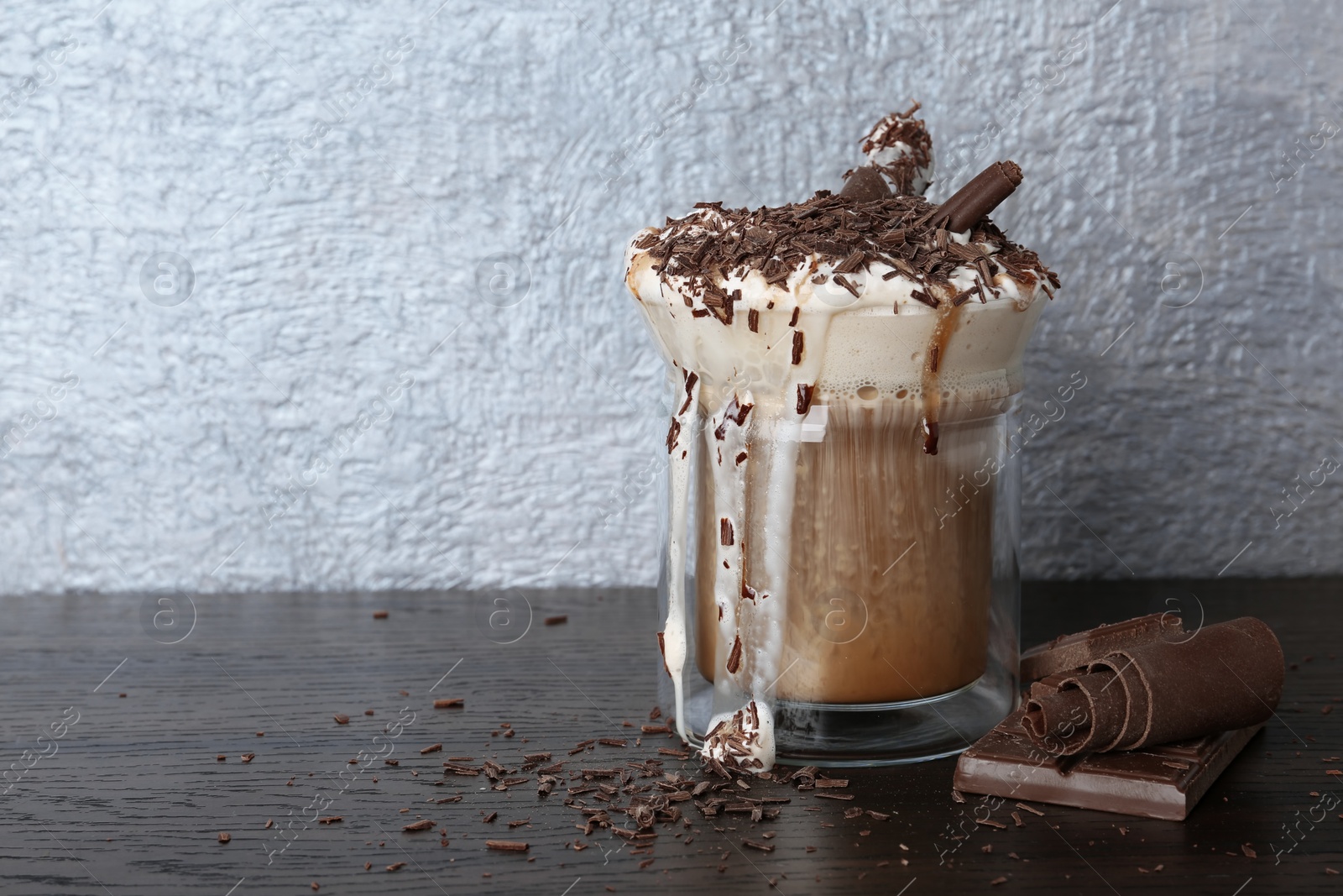 Photo of Glass cup of tasty coffee with whipped cream and chocolate on wooden table. Space for text