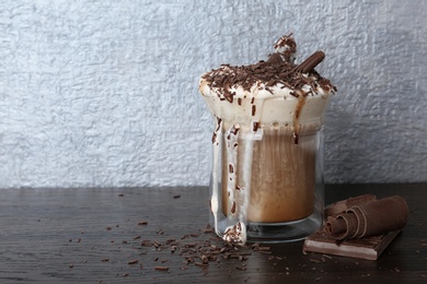 Photo of Glass cup of tasty coffee with whipped cream and chocolate on wooden table. Space for text