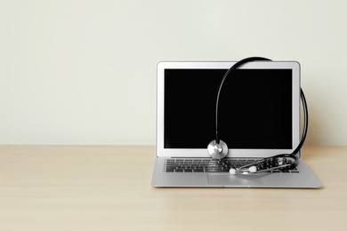 Photo of Laptop with blank screen and stethoscope on table against light background, space for text. Computer repair