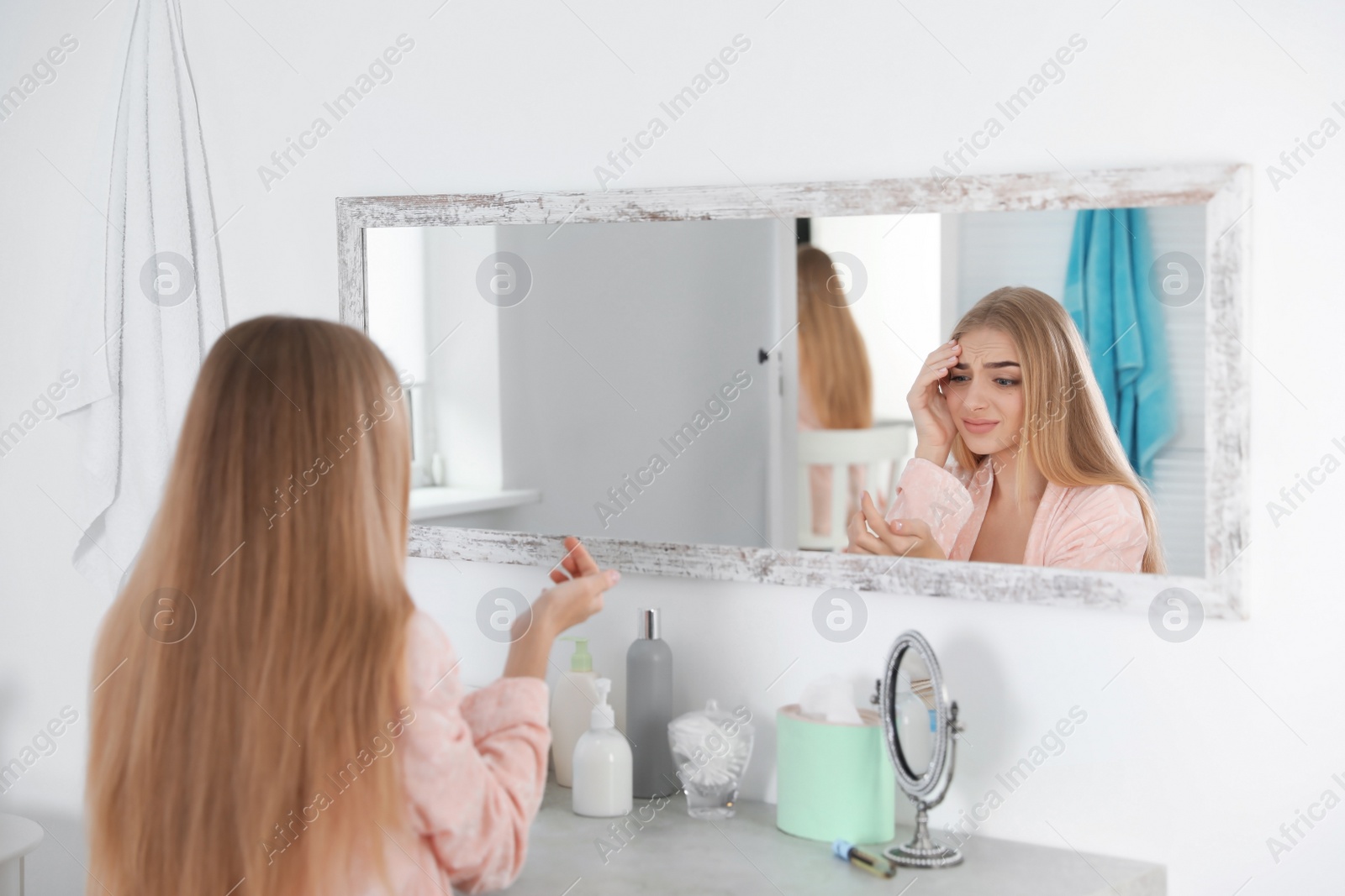 Photo of Young woman with eyelash loss problem looking in mirror indoors