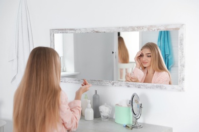 Young woman with eyelash loss problem looking in mirror indoors