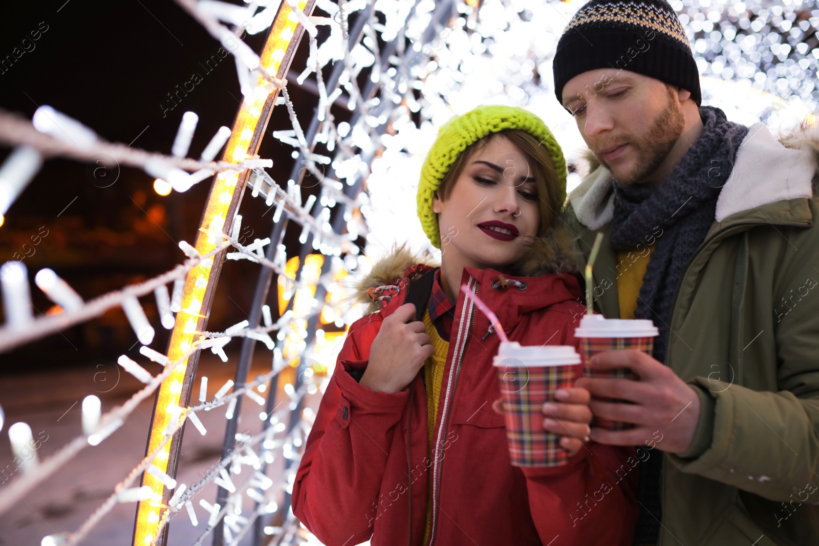 Photo of Young couple with cups of mulled wine at winter fair. Space for text