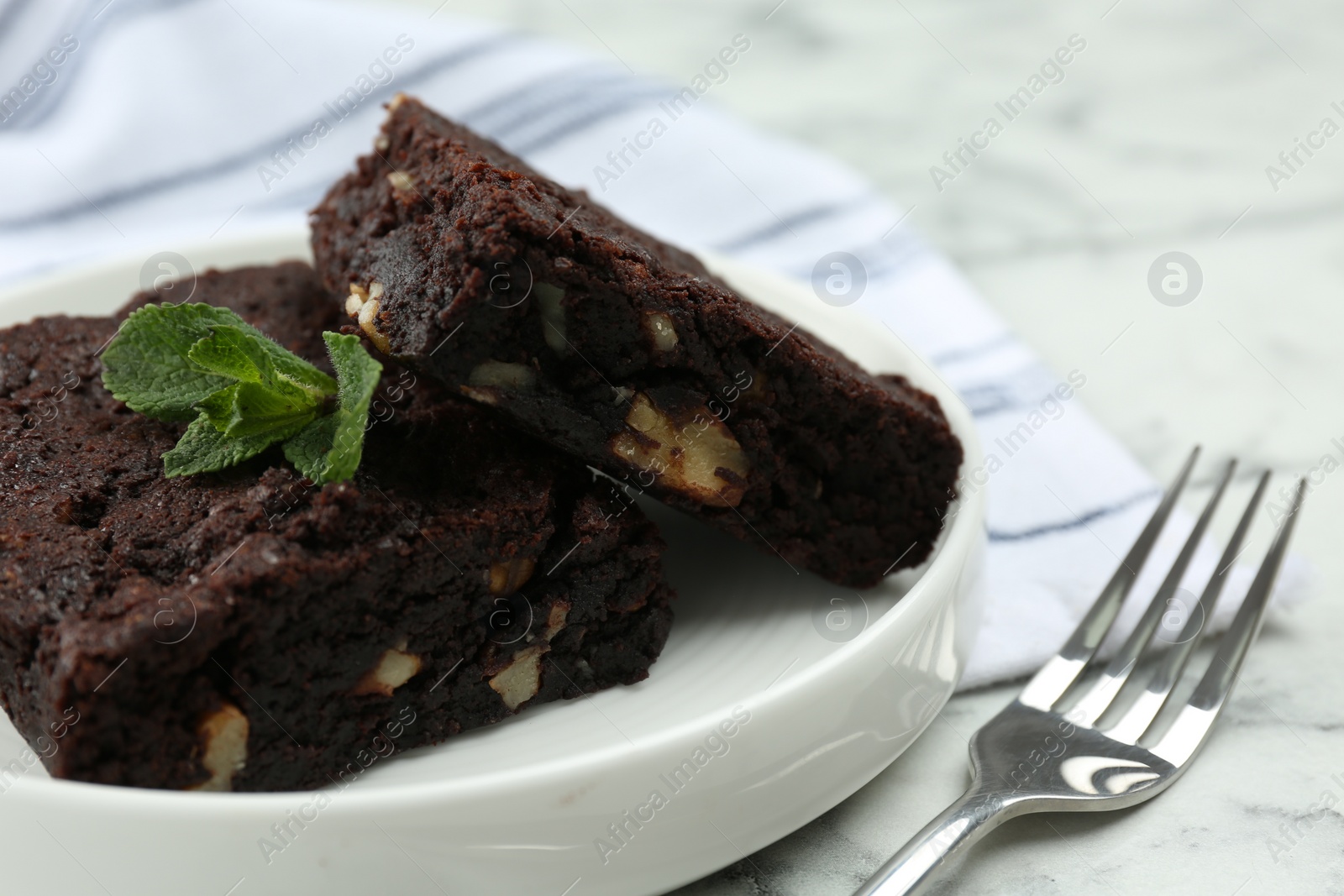 Photo of Delicious brownies with nuts and mint on white marble table, closeup