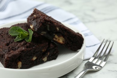 Photo of Delicious brownies with nuts and mint on white marble table, closeup