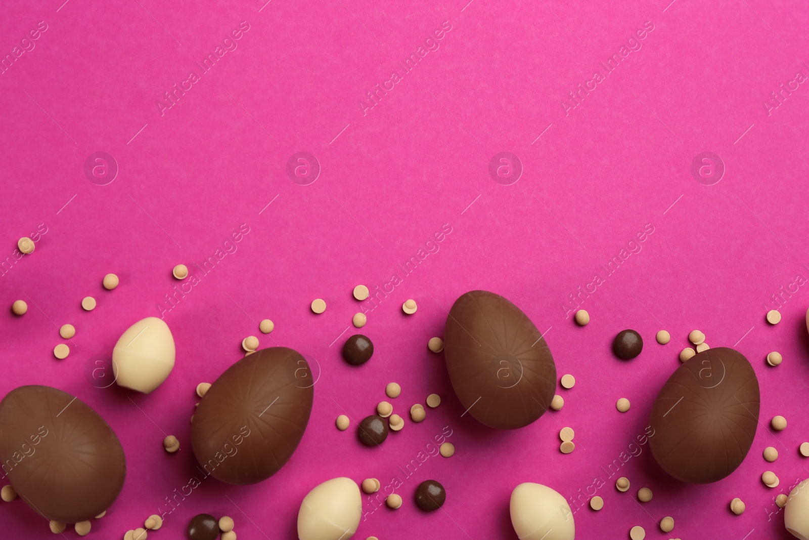 Photo of Sweet chocolate eggs and candies on pink background, flat lay. Space for text