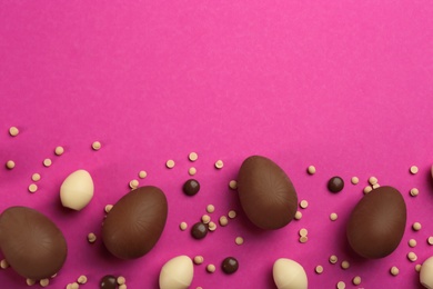 Sweet chocolate eggs and candies on pink background, flat lay. Space for text