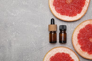 Photo of Bottles of essential oil with grapefruit slices on grey table, flat lay. Space for text