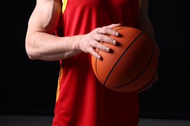 Photo of Athletic man with basketball ball on black background, closeup