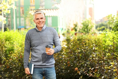 Photo of Handsome mature man with coffee and book in park. Space for text