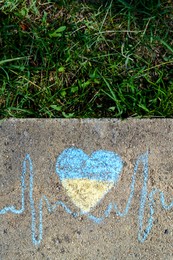 Photo of Cardiogram line with heart drawn by blue and yellow chalk on asphalt near green grass, top view