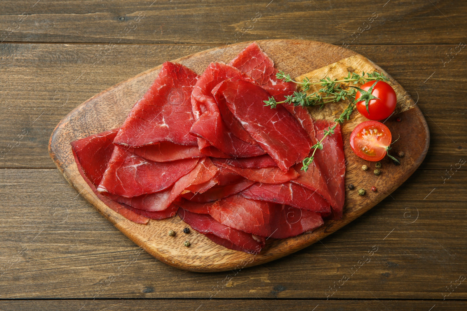 Photo of Tasty bresaola, peppercorns, tomatoes and thyme on wooden table, top view