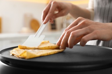 Woman cooking delicious crepe on electric pancake maker in kitchen, closeup