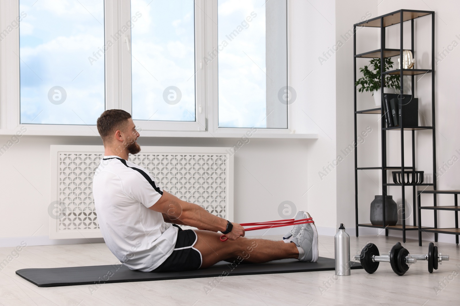 Photo of Athletic man doing exercise with elastic resistance band on mat at home