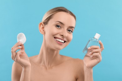 Photo of Removing makeup. Smiling woman with cotton pad and bottle on light blue background