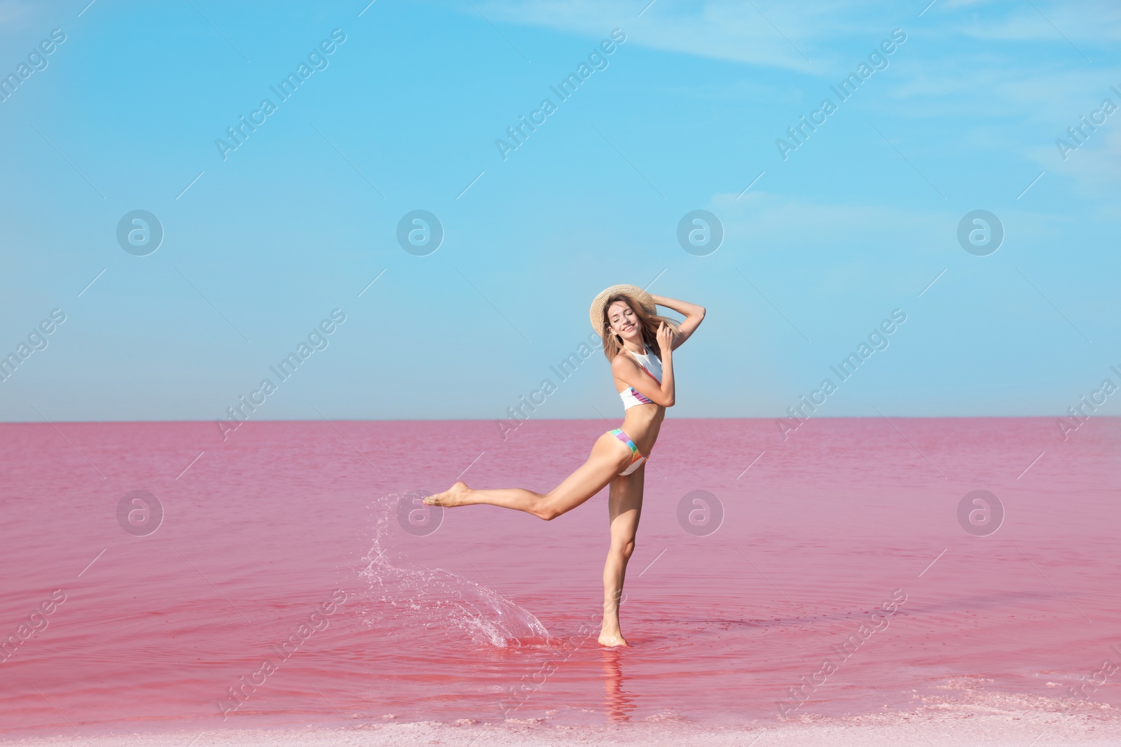 Photo of Beautiful woman in swimsuit standing near pink lake on sunny day