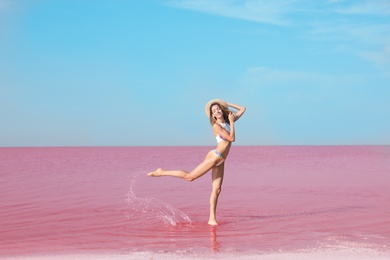 Beautiful woman in swimsuit standing near pink lake on sunny day