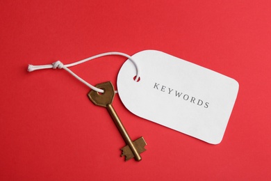 Photo of Metal key and tag wIth word KEYWORDS on red background, top view