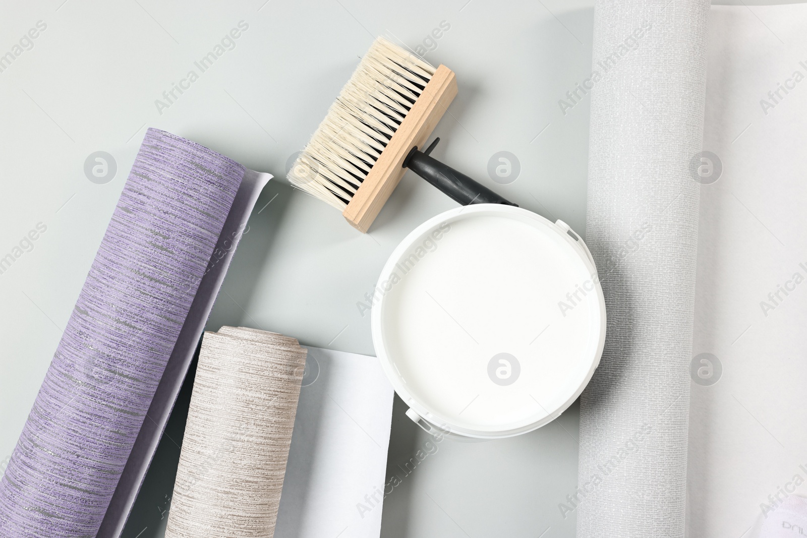 Image of Wallpaper rolls, brush and bucket of glue on light grey background, flat lay
