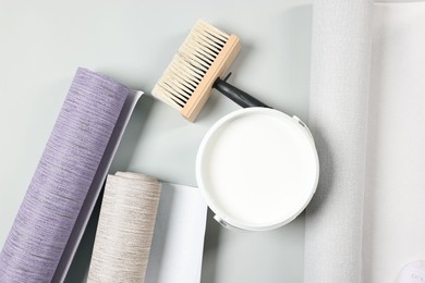 Wallpaper rolls, brush and bucket of glue on light grey background, flat lay