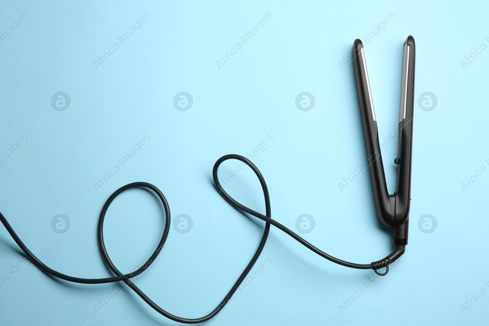 Photo of Modern flat hair iron on light blue background, top view