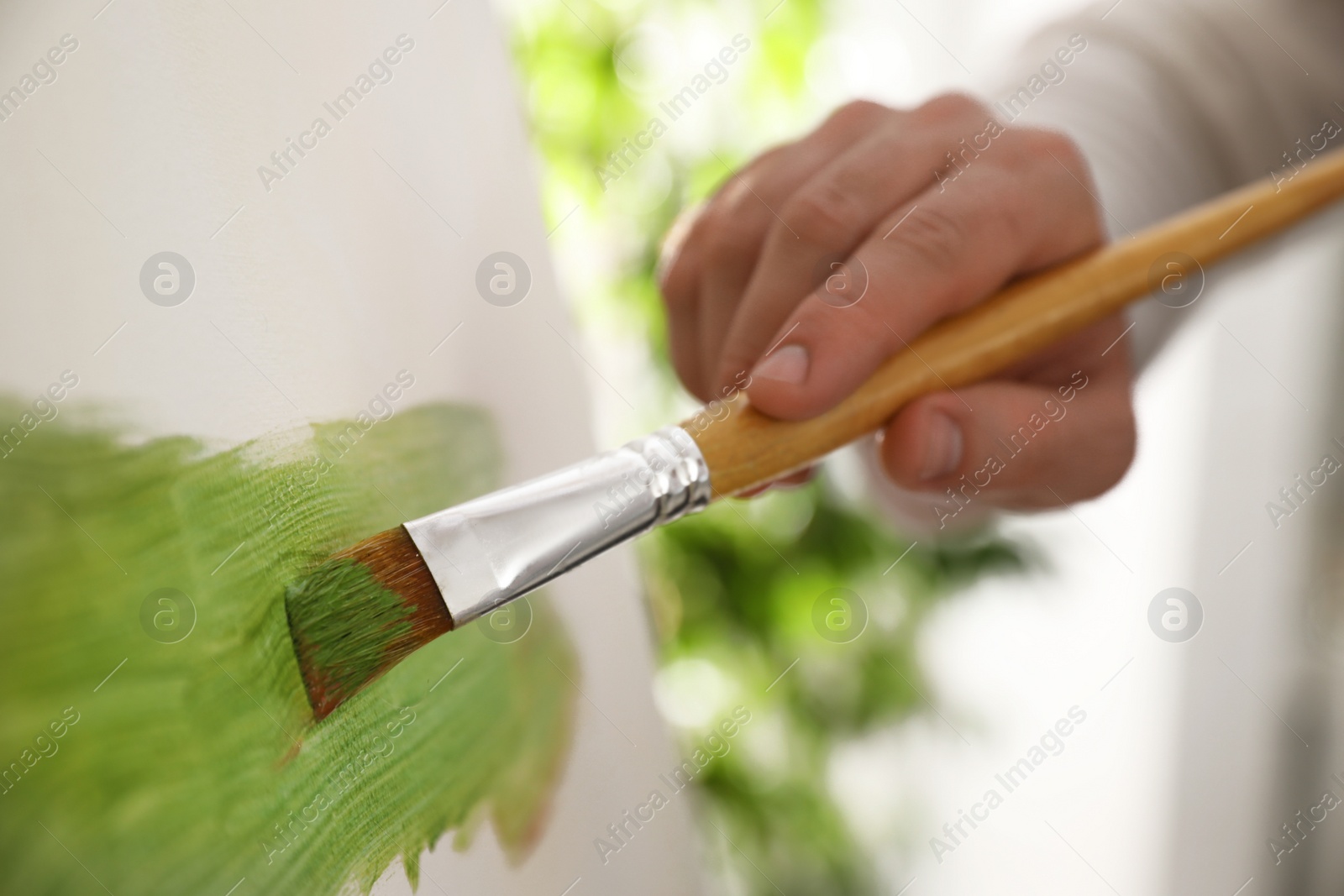 Photo of Young man painting on easel with brush in artist studio, closeup