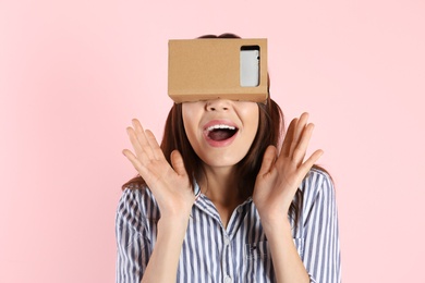 Young woman using cardboard virtual reality headset on color background