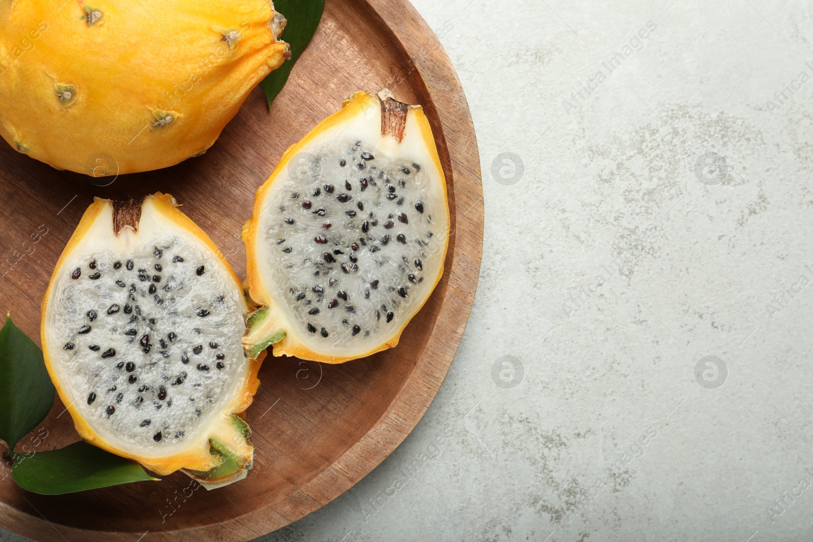 Photo of Wooden plate with delicious cut and whole dragon fruits (pitahaya) on grey table, top view. Space for text