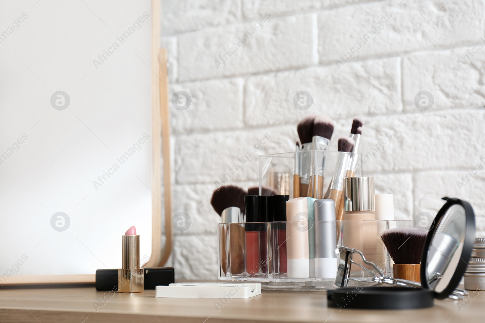 Photo of Organizer with cosmetic products for makeup on table near brick wall