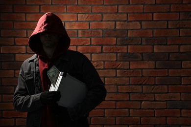 Thief in hoodie with briefcase of money against red brick wall. Space for text