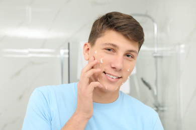 Teen guy with acne problem applying cream in bathroom