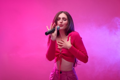 Beautiful woman with microphone singing on pink background