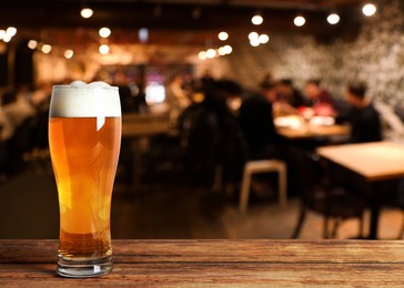 Image of Glass with cold tasty beer on wooden table in pub, space for text
