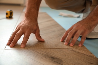 Photo of Professional worker installing new parquet flooring indoors, closeup